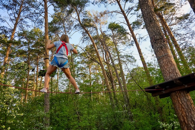 Photo young girl in denim shorts deftly walks on rope holding on to rope with hands