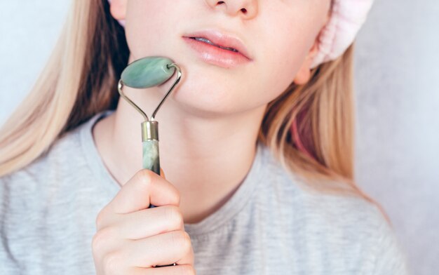 Ragazza che fa massaggio facciale guasha tradizionale cinese, routine di cura della pelle domestica