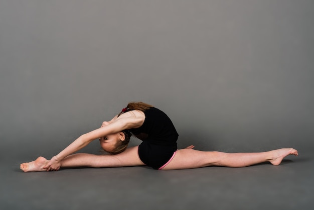 Ragazza giovane facendo ginnastica su uno sfondo grigio, studio