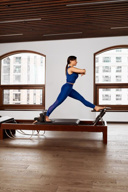 Young girl doing pilates exercises with a reformer bed. Beautiful slim fitness trainer on reformer. Fitness concept