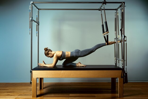 Young girl doing pilates exercises with a reformer bed beautiful slim fitness trainer on reformer