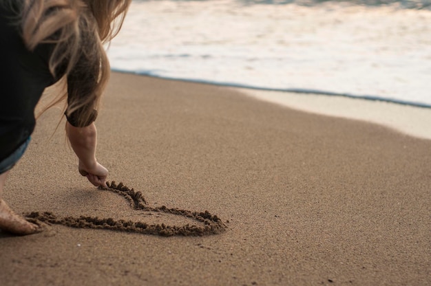 La ragazza disegna un cuore in sabbia che si siede sulla spiaggia