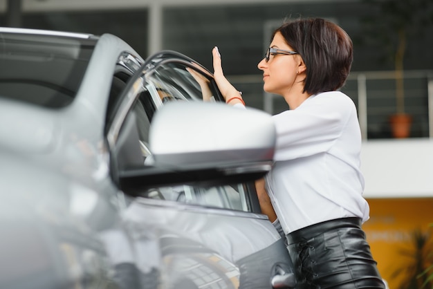 Foto giovane ragazza che sogna di un'auto nuova ispezionando una nuova macchina bianca presso una concessionaria di automobili