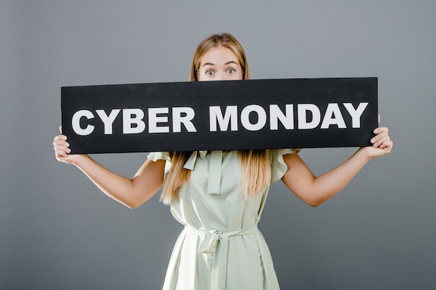 Young girl in dress covers her mouth with cyber monday sign isolated over grey