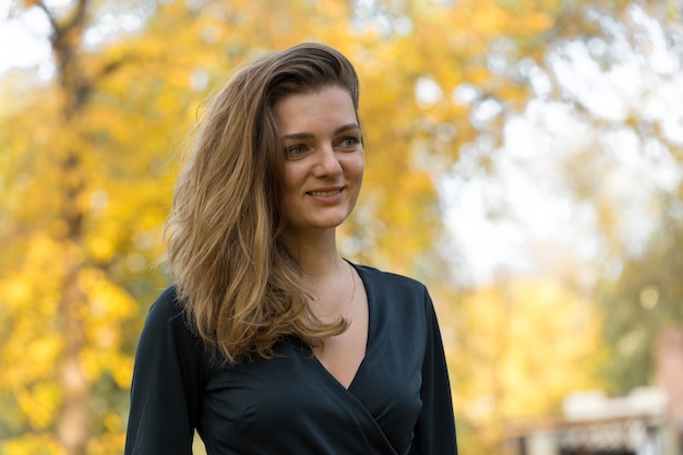 A young girl in dress poses in a park on a background of golden autumn foliage.