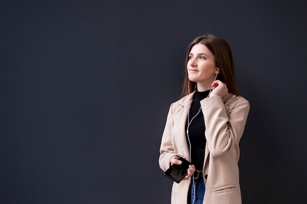 young girl dressed in jeans and a coat standing and listening to music