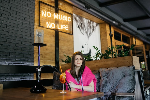 Young girl drinking aperol Aperol spritz cocktail in a glass The girl smokes a hookah Hookah in a restaurant Woman smokes a hookah and sits on a chair