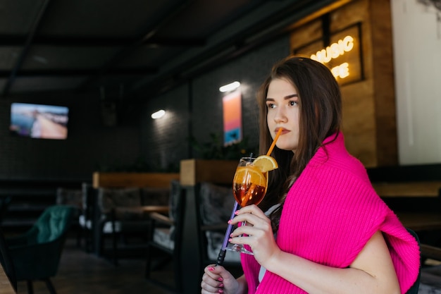 Young girl drinking aperol Young girl drinking a cocktail in a restaurant Cocktail in hands Cocktail aperol spritz in a glass