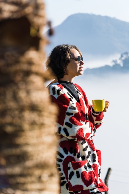 写真 寒い日にマグカップからコーヒーを飲む少女霧と雲が街の景色を覆っている