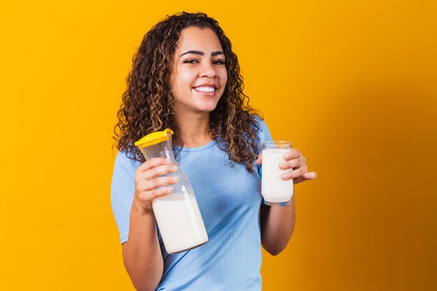 Молодая девушка пьет стакан молока и держит полную бутылку.