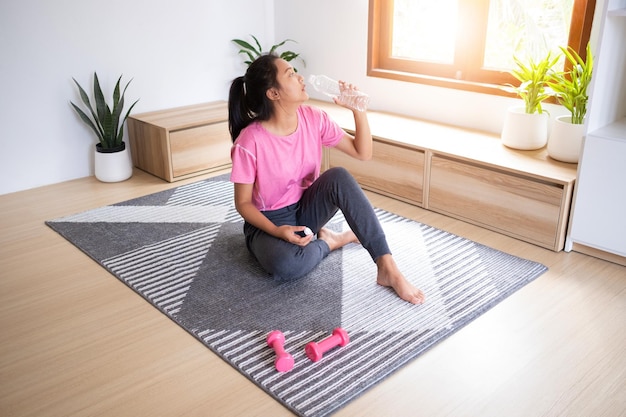 Young girl drinking water after excercise at home in living roomAsian girl