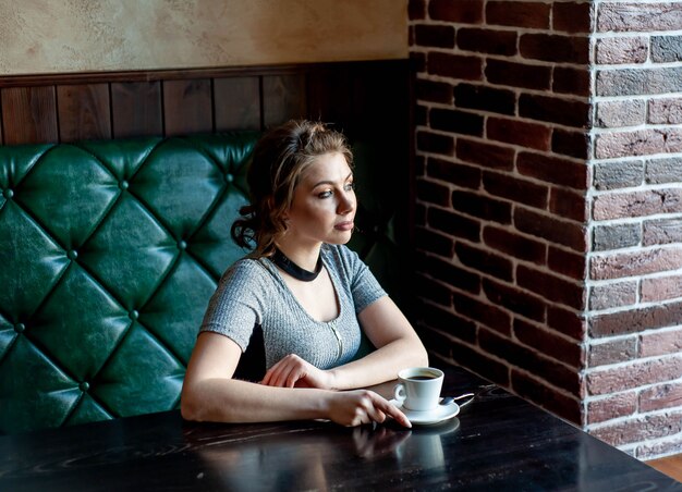 young girl drinks coffee sitting on a sofa near the window