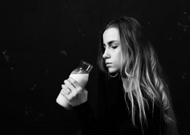 Young girl drinks milk from a bottle on a black wall background