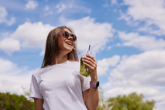 Молодая девушка пьет освежающий коктейль крупным планом на фоне неба