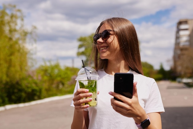 若い女の子は、空を背景にさわやかなカクテルのクローズ アップを飲みます