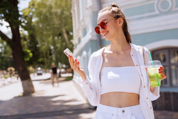 A young girl drinks a summer refreshing cocktail in the city and takes a selfie