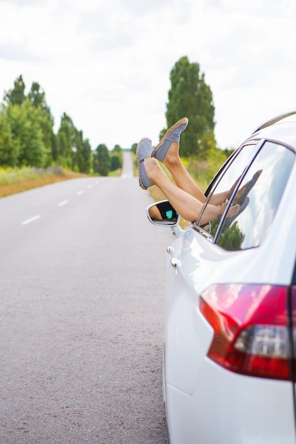 窓から足を引っ張って車を運転している若い女の子が車輪の後ろで休んでいるロードトリップ