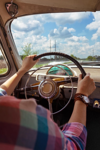 Young girl driving a retro car by the road at the fields