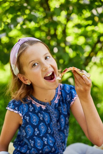 Foto ragazza che gode di una fetta di pizza all'aperto in una giornata di sole