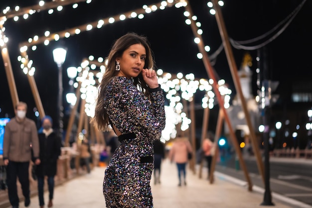 Young girl in a fashionable dress with sequins in the city christmas lights