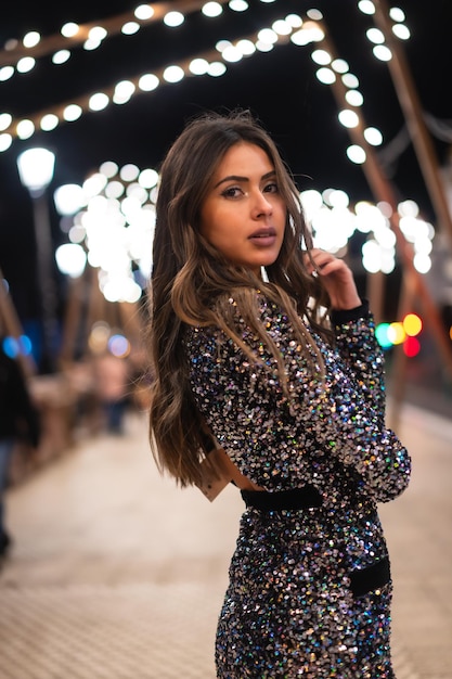 Young girl in a fashionable dress with sequins in the city christmas lights