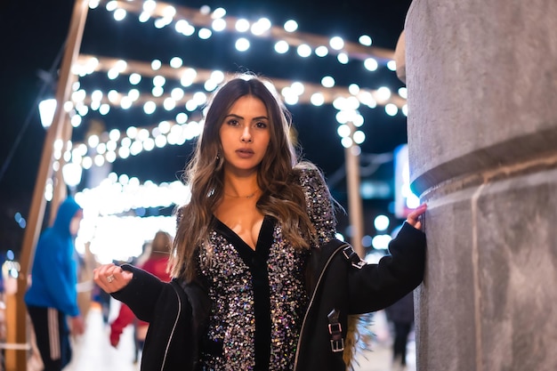 Giovane ragazza in un vestito alla moda con paillettes nelle luci di natale della città