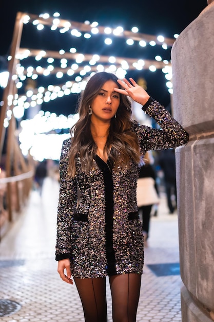 Giovane ragazza in un vestito alla moda con paillettes nelle luci di natale della città