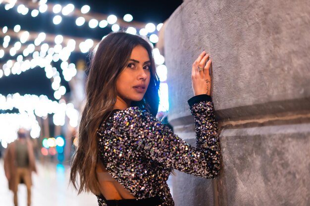 Young girl in a fashionable dress with sequins in the city christmas lights