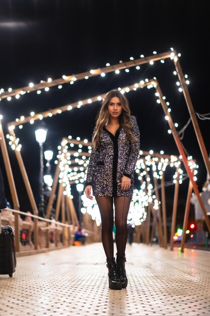 Young girl in a fashionable dress with sequins in the city christmas lights