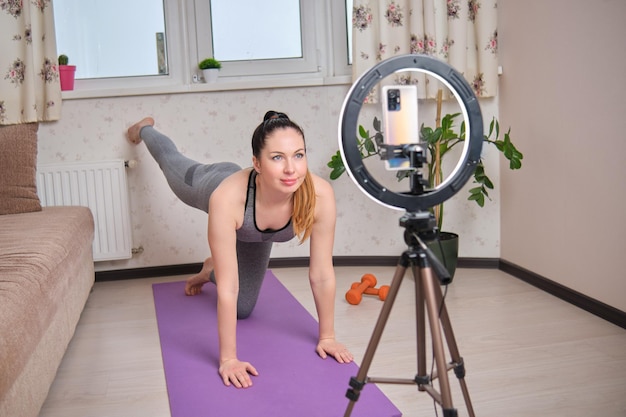 Young girl fitness trainer conducts a live broadcast of a workout using a smartphone
