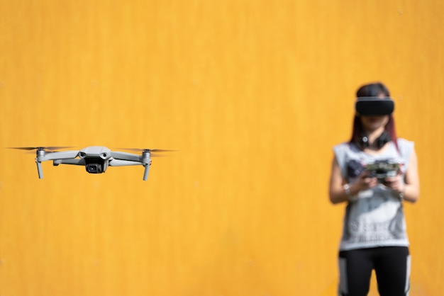 Young girl flying a drone with VR glasses in a yellow background