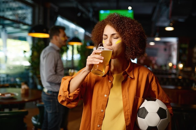 Young girl football fan drinking beer while rest in sports bar with friends