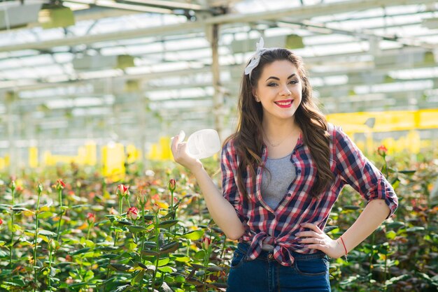 A young girl gardener or greenhouse worker takes care of flowers and waters them in the greenhouse