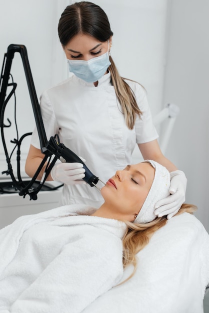 A young girl gets a charcoal peeling for the skin of the face in a beauty salon Laser pulses cleanse the skin Hardware cosmetology The process of photothermolysis warming the skin