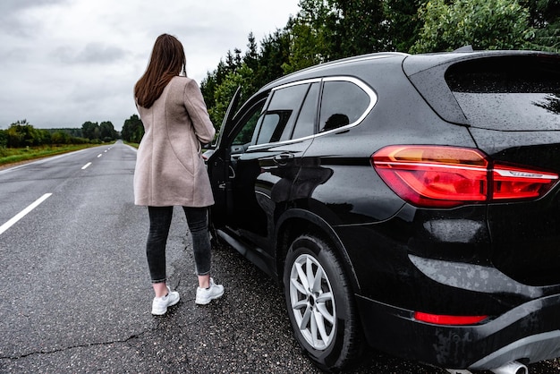 Young girl getting into a car on the road in rainy weather.