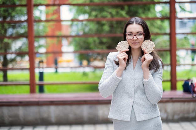 A young girl in glasses eating round bread on the street