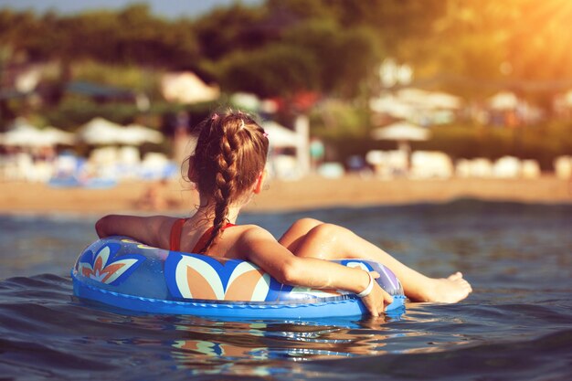 안경을 쓴 어린 소녀는 뜨거운 햇살 가득한 여름에 팽창식 도넛 위에서 물놀이를 한다