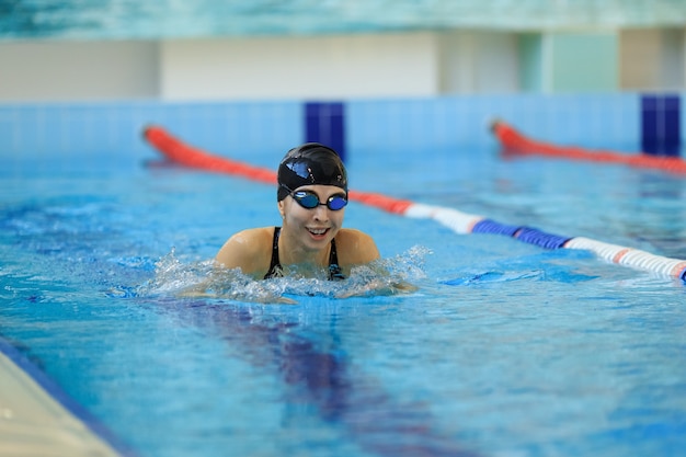 Young girl in goggles and cap swimming butterfly stroke style
in the blue water pool.