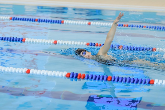 Young girl in goggles and cap swimming front crawl stroke style\
in the blue water pool.