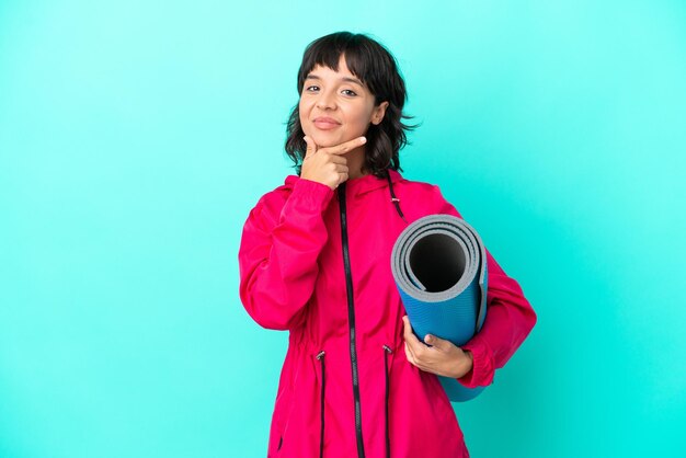 Young girl going to yoga classes while holding a mat isolated on blue background thinking