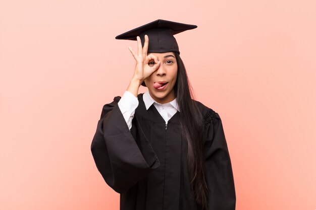 young girl in graduating robe joking and looking through peephole