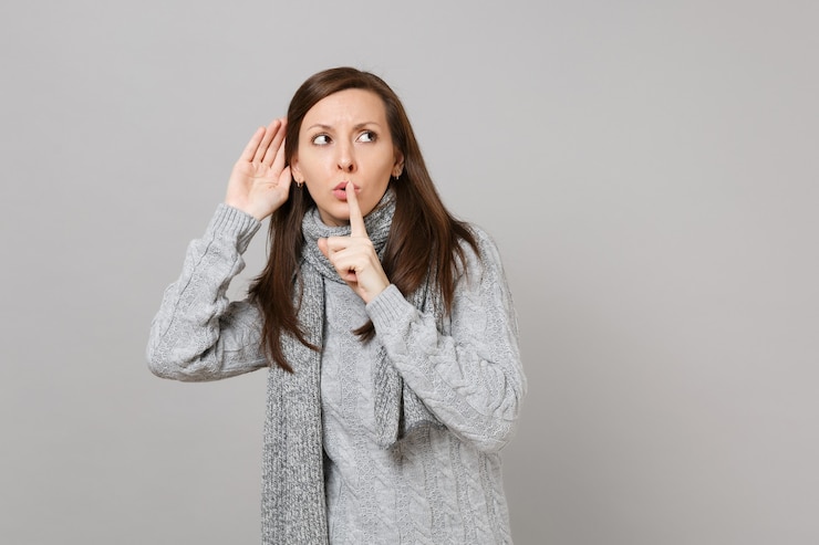 Photo young girl in gray sweater scarf saying hush be quiet with finger on lips shhh gesture eavesdrop and hearing isolated on grey background. healthy fashion lifestyle people emotions cold season concept.