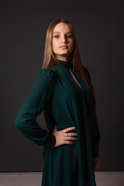 A young girl in a green strict dress poses in a photo studio on a gray background