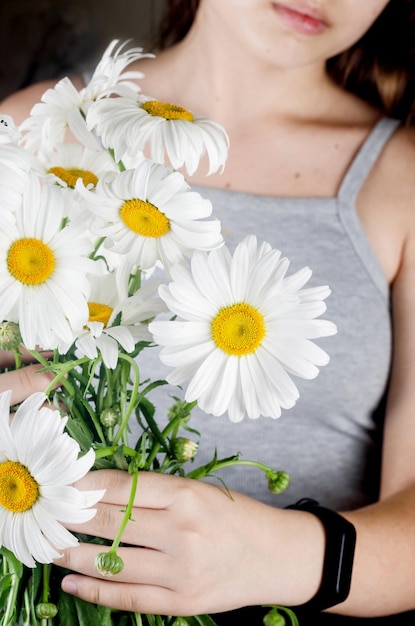 The Young girl in a grey dress holds a bouquet of white  daisies in her hands. Summer flowers Chamomile. in tender hands. Image with selective focus.