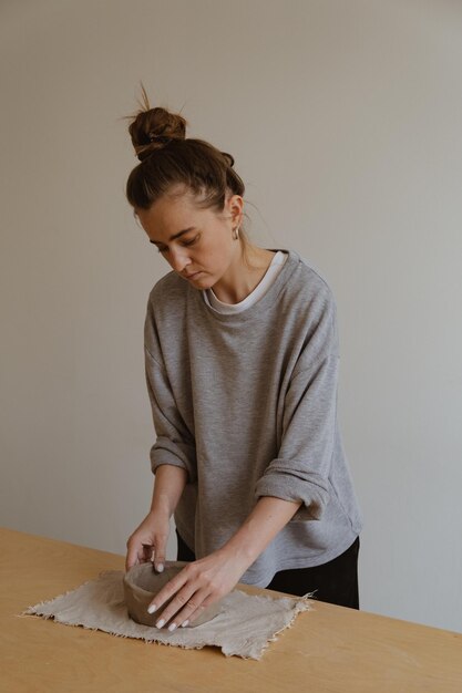 Photo a young girl in a grey long sleeve makes a vase of clay with her own hands in a sculpture workshop