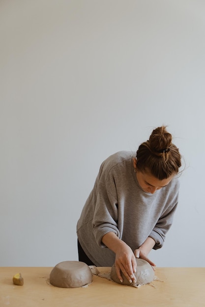 A young girl in a grey long sleeve makes a vase of clay with her own hands in a sculpture workshop