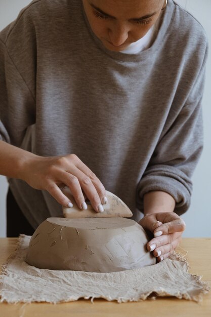 灰色の長袖の少女は、彫刻のワークショップで自分の手で粘土の花瓶を作ります