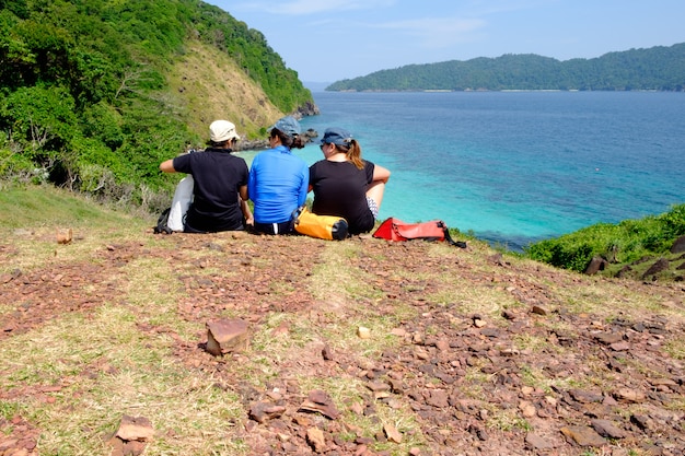 若い女の子グループは崖の上に座る、山と青い空と海の風景