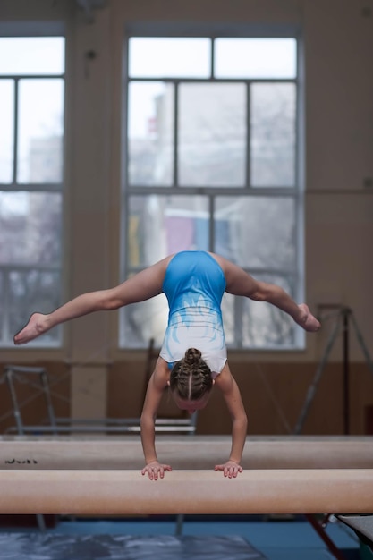 Молодая гимнастка выполняет стойку на руках на бревне