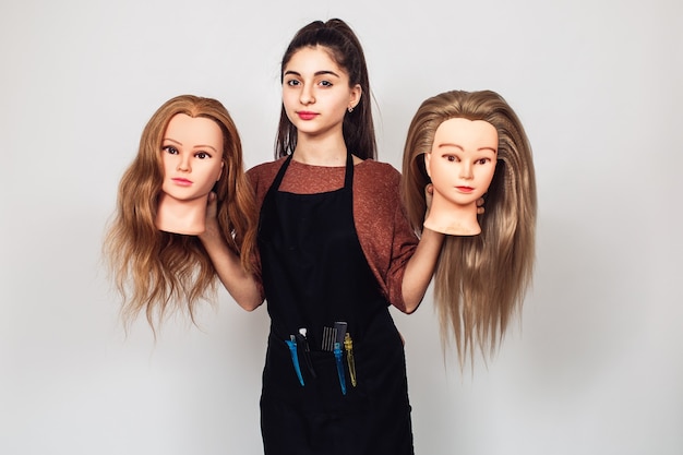 Young girl hairdresser holds in hands two mannequin heads.